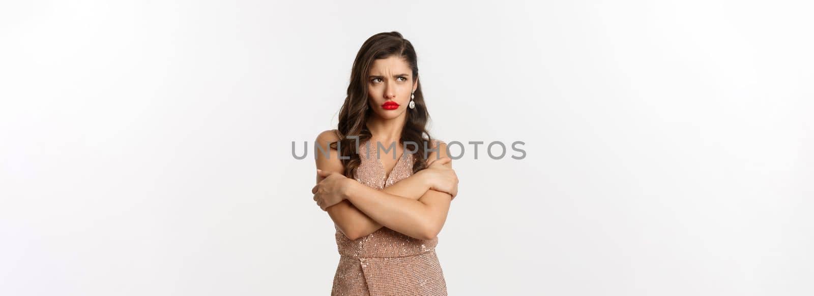 Celebration and party concept. Sulking woman looking angry, dressed for formal event in glamour dress, hugging herself and pouting upset, white background.