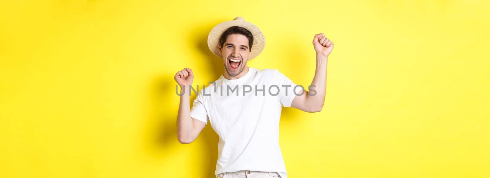 Concept of tourism and lifestyle. Happy man tourist celebrating, rejoicing over vacation, standing over yellow background.