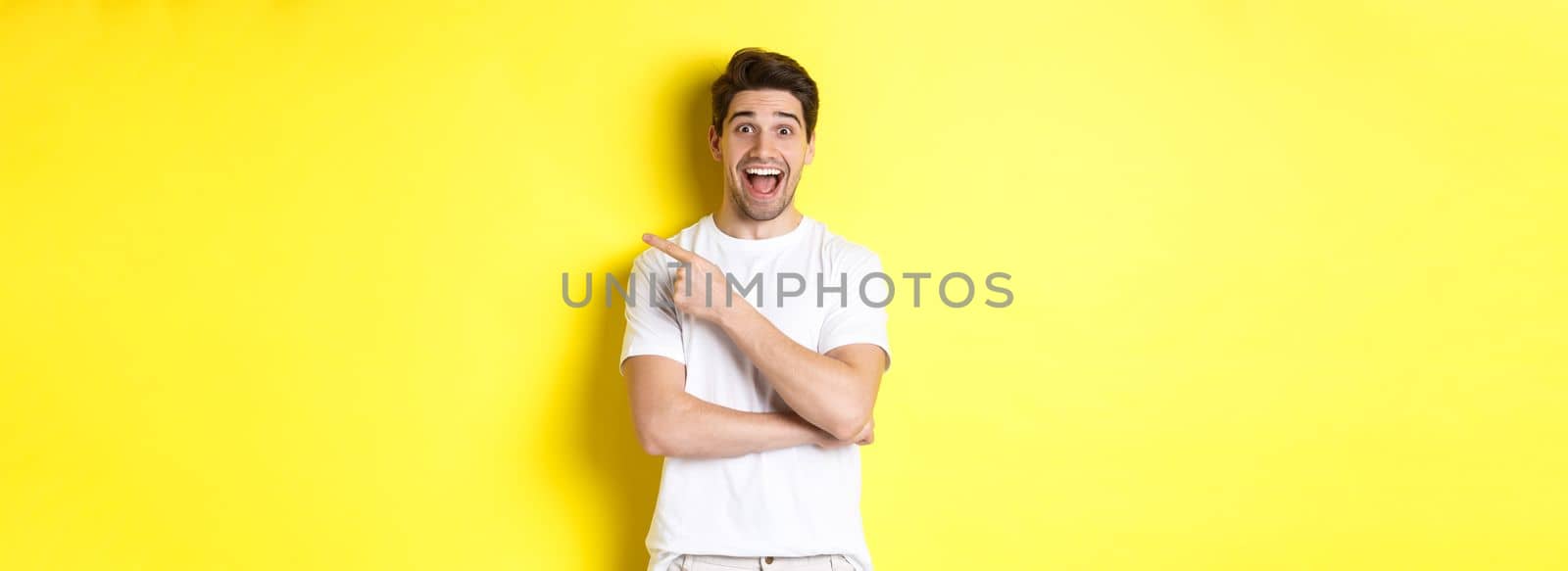 Image of excited smiling man showing black friday offers, pointing finger right and looking amazed, standing over yellow background.