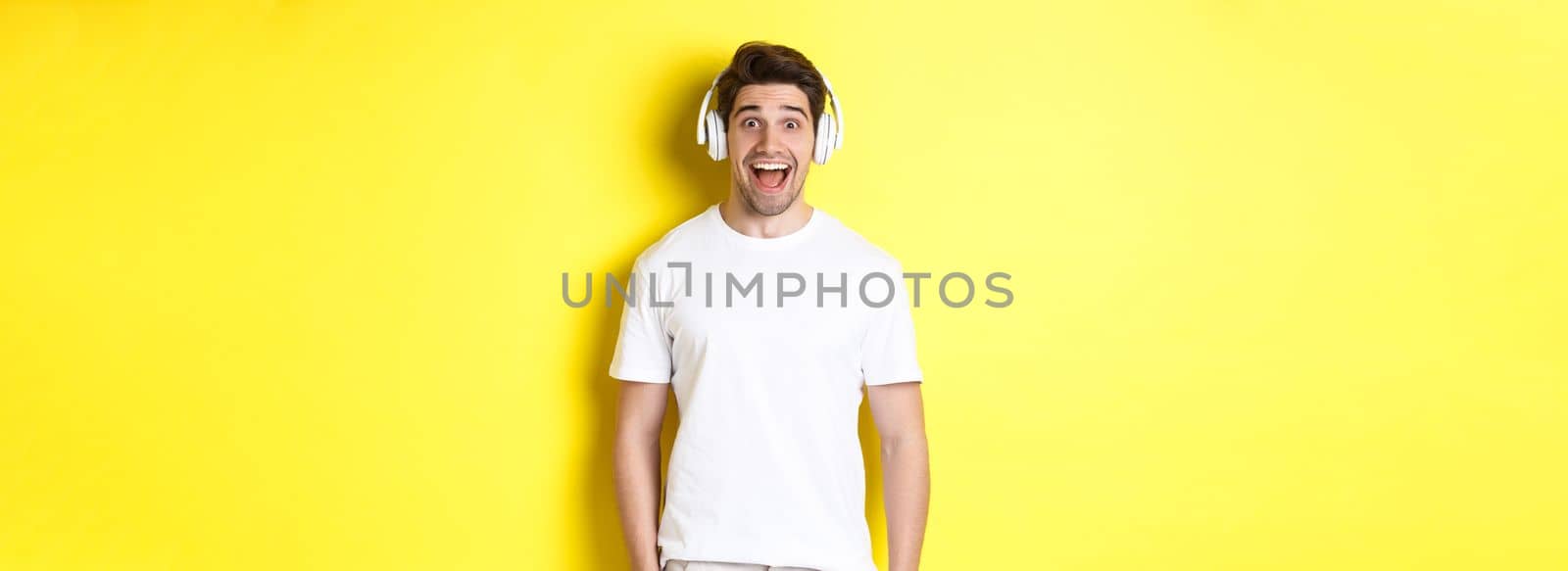 Man in headphones looking surprised, standing against yellow background in white outfit by Benzoix