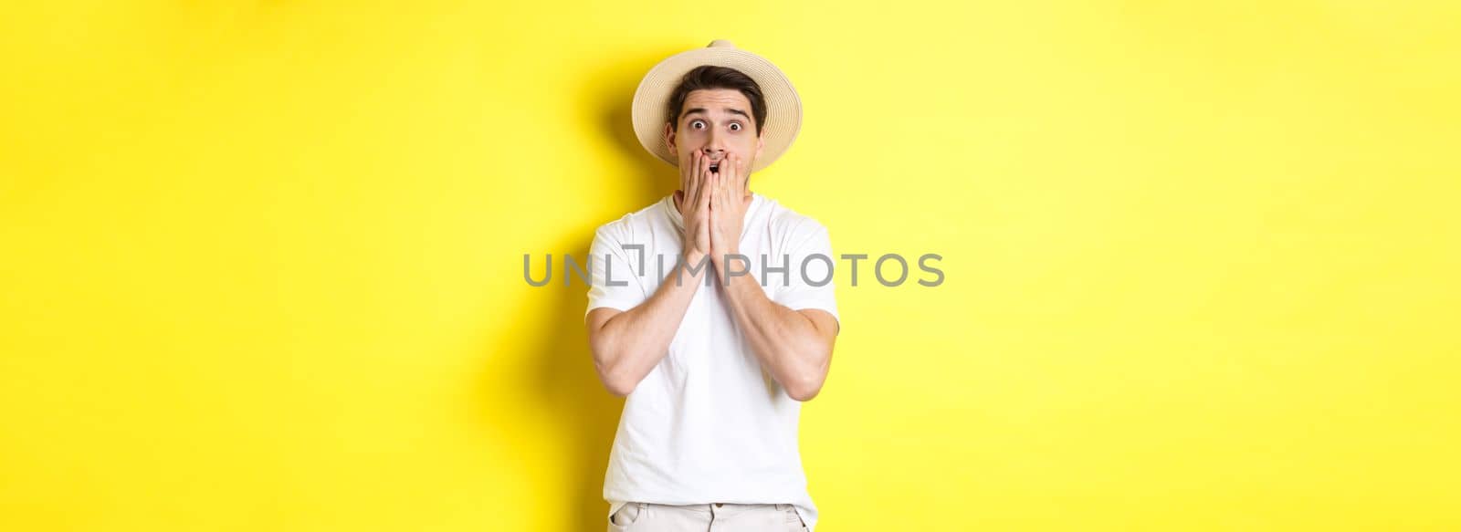 Concept of tourism and summer. Shocked guy jumping from fear, standing startled against yellow background.