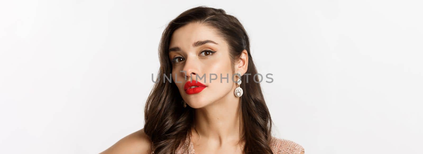Concept of New Year celebration and winter holidays. Close-up of sensual and beautiful woman with red lips, looking confident at camera, wearing luxury earrings, white background.