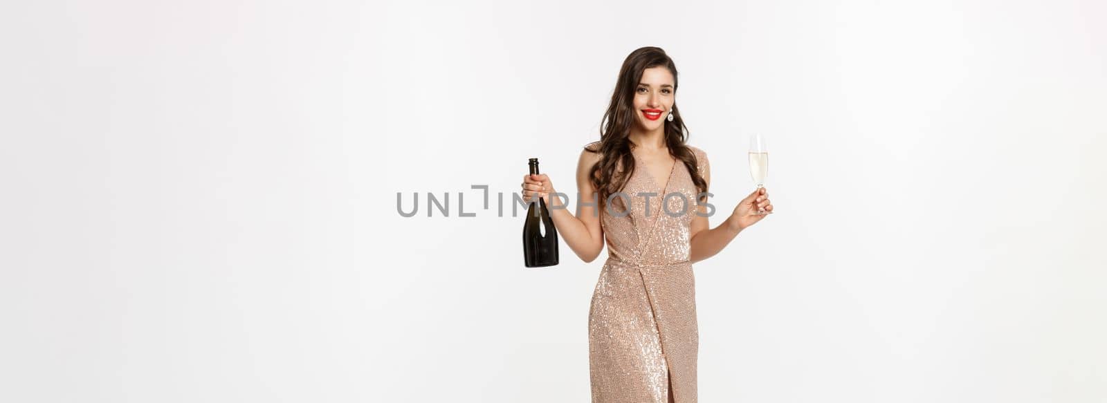 Christmas party and celebration concept. Full length of elegant woman with red lips, luxury dress, holding glass of champagne and bottle, white background.