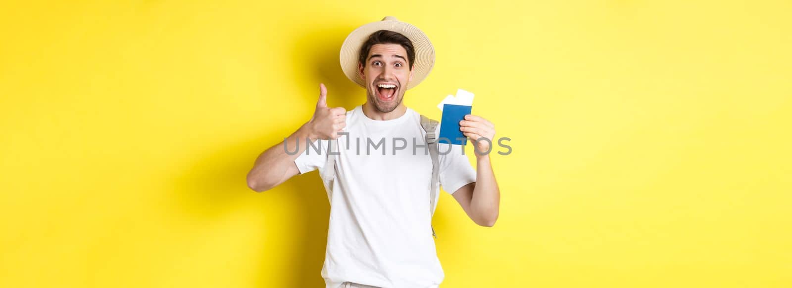 Tourism and vacation. Satisfied male tourist showing passport with tickets and thumb up, recommending travel company, standing over yellow background by Benzoix