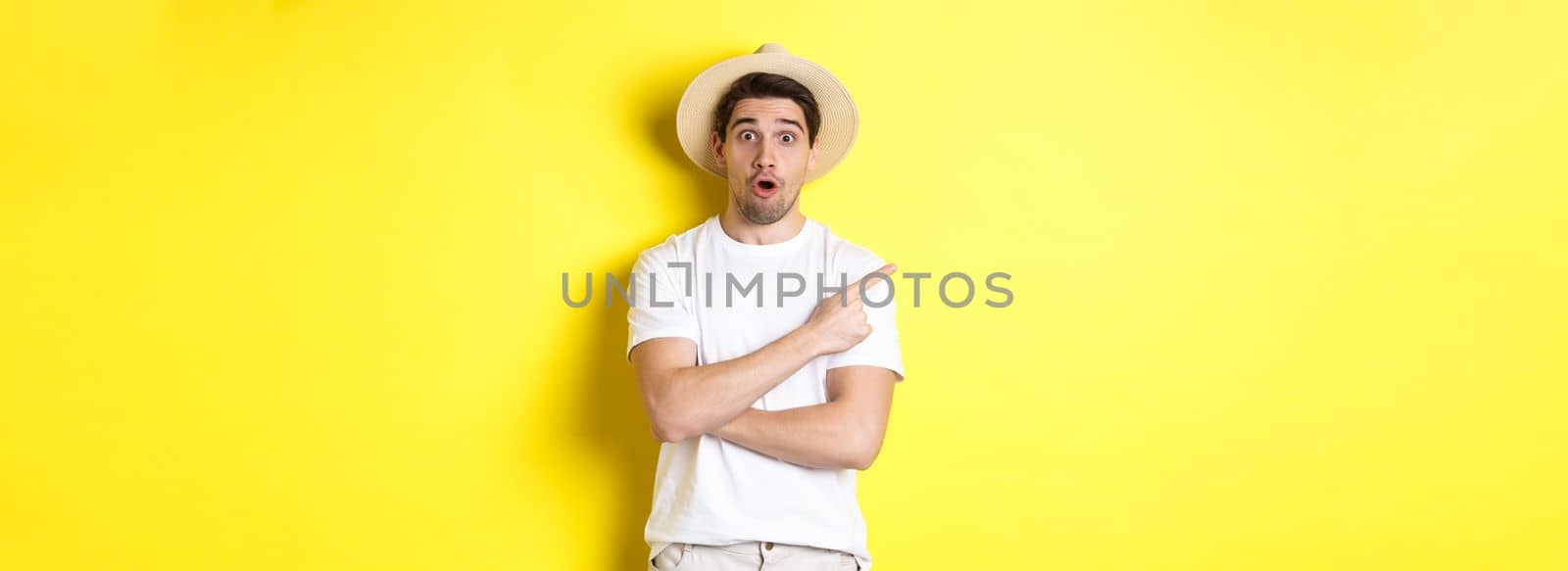 Concept of tourism and lifestyle. Surprised handsome man tourist pointing finger left, looking impressed about promo offer, yellow background.