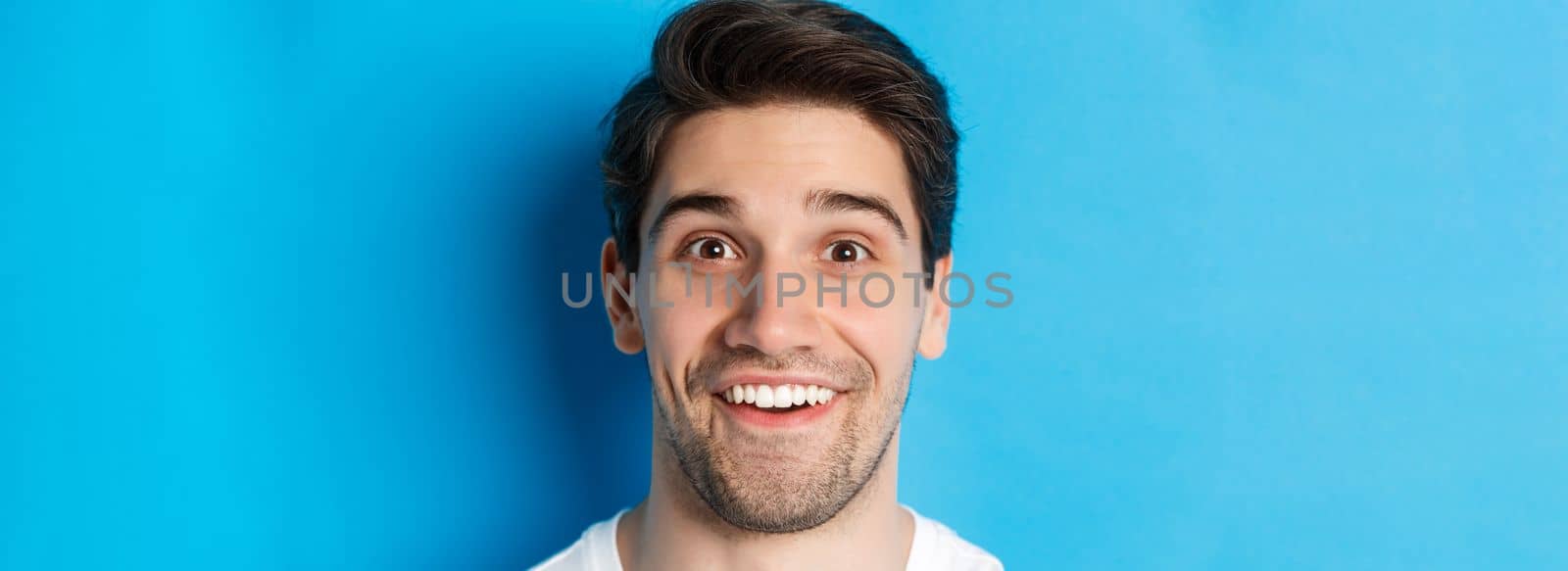 Head shot of handsome male model looking amazed, smiling wondered, standing over blue background by Benzoix