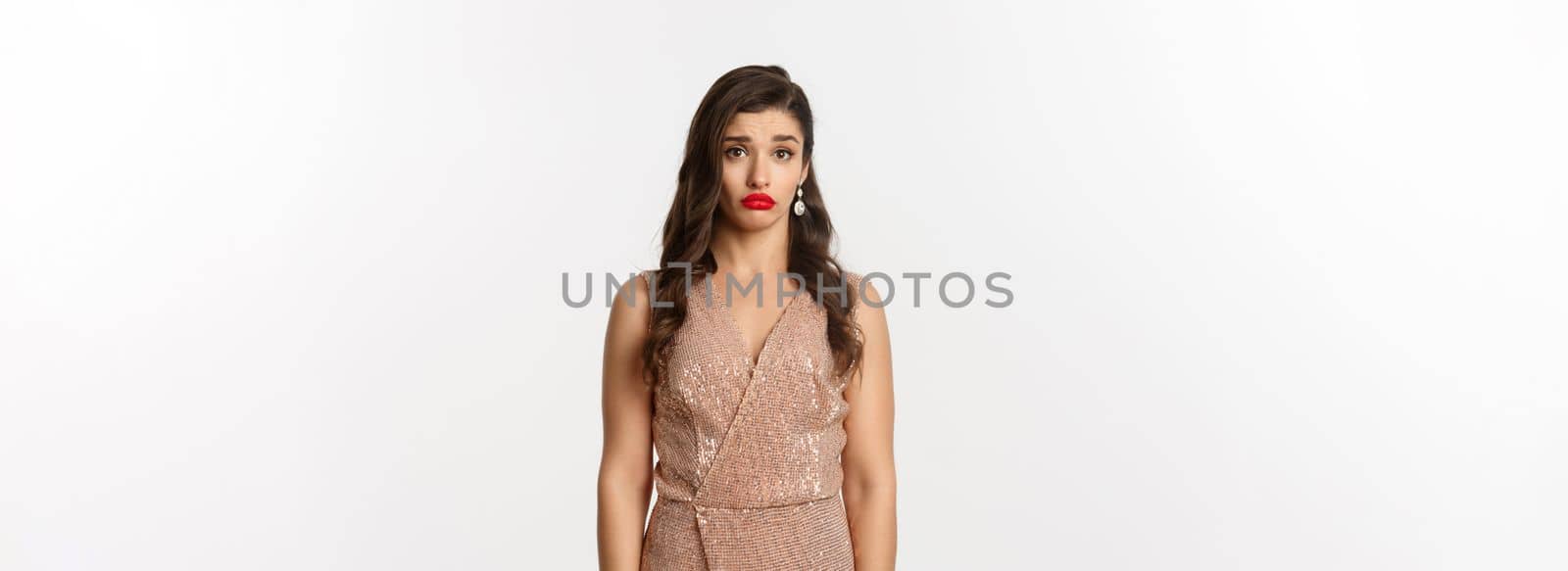 Celebration and party concept. Sad and confused young woman in glamour dress staring at camera distressed, standing against white background.