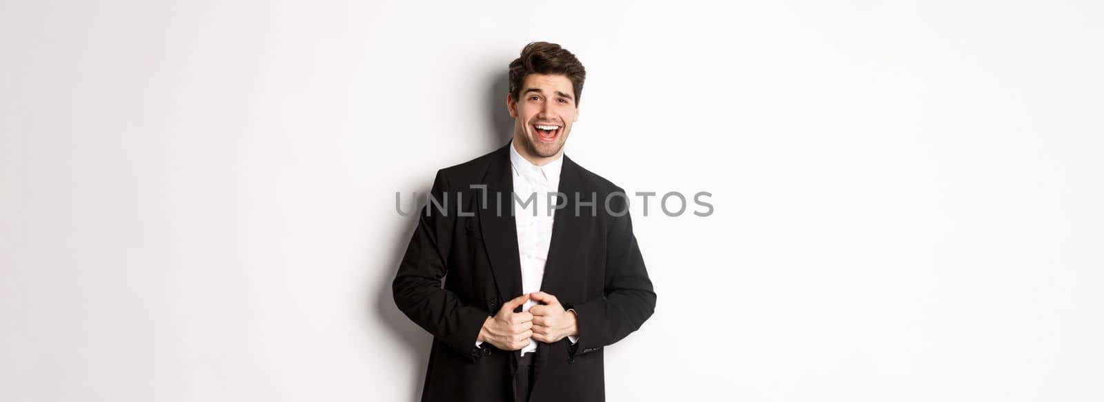 Concept of new year party, celebration and lifestyle. Portrait of handsome and confident man in suit, smiling pleased, feeling successful, standing over white background.