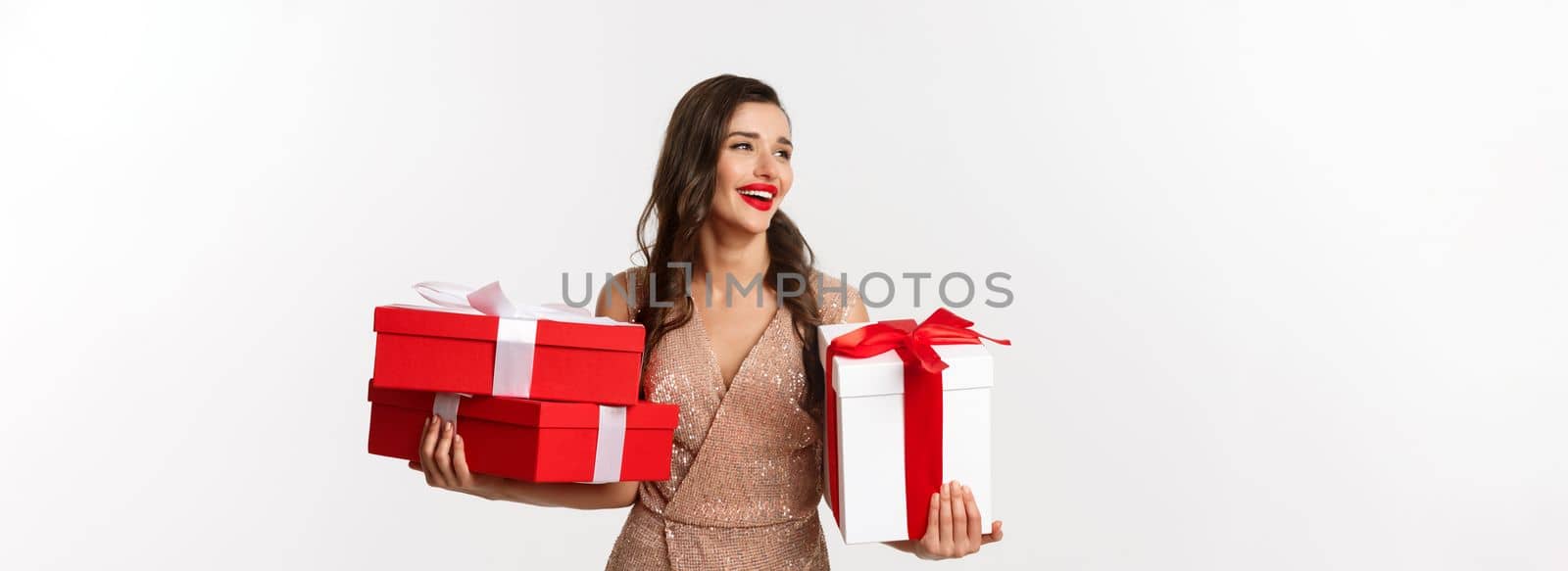 Holidays, celebration concept. Elegant woman with red lips, luxury dress, holding Christmas presents and smiling, enjoying New Year eve, white background.