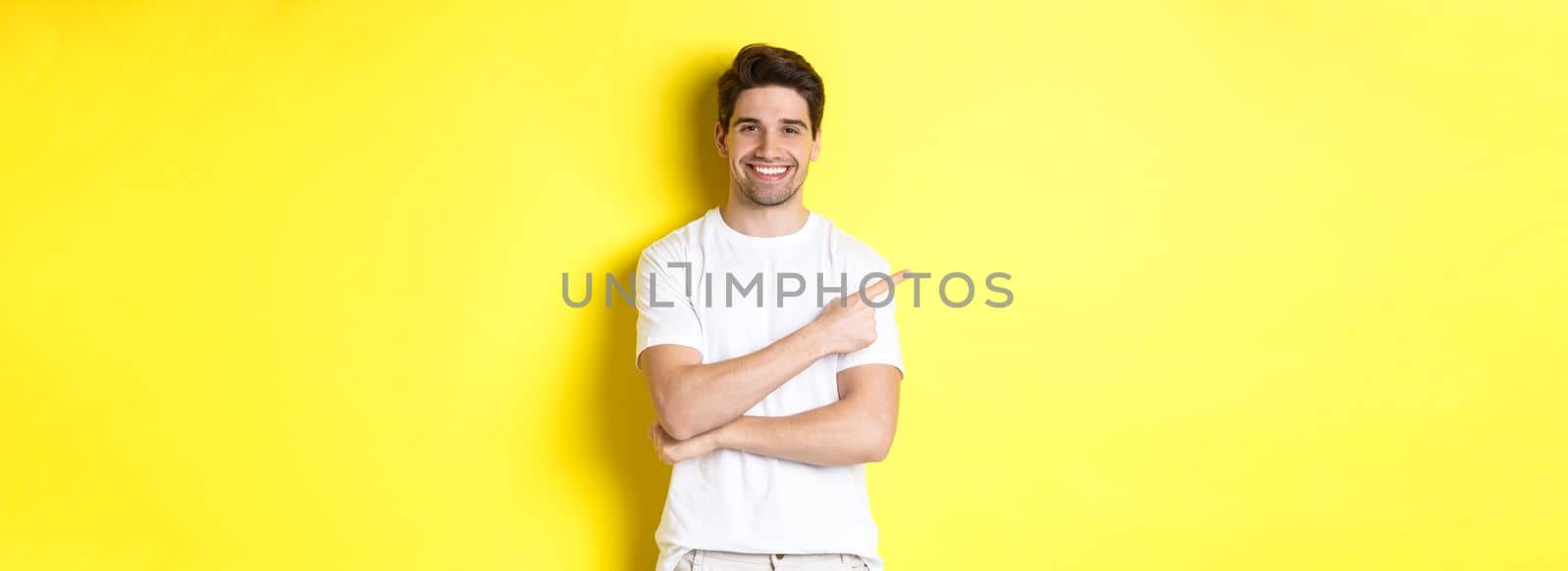 Handsome guy pointing left and smiling, showing advertisement on yellow copy space.