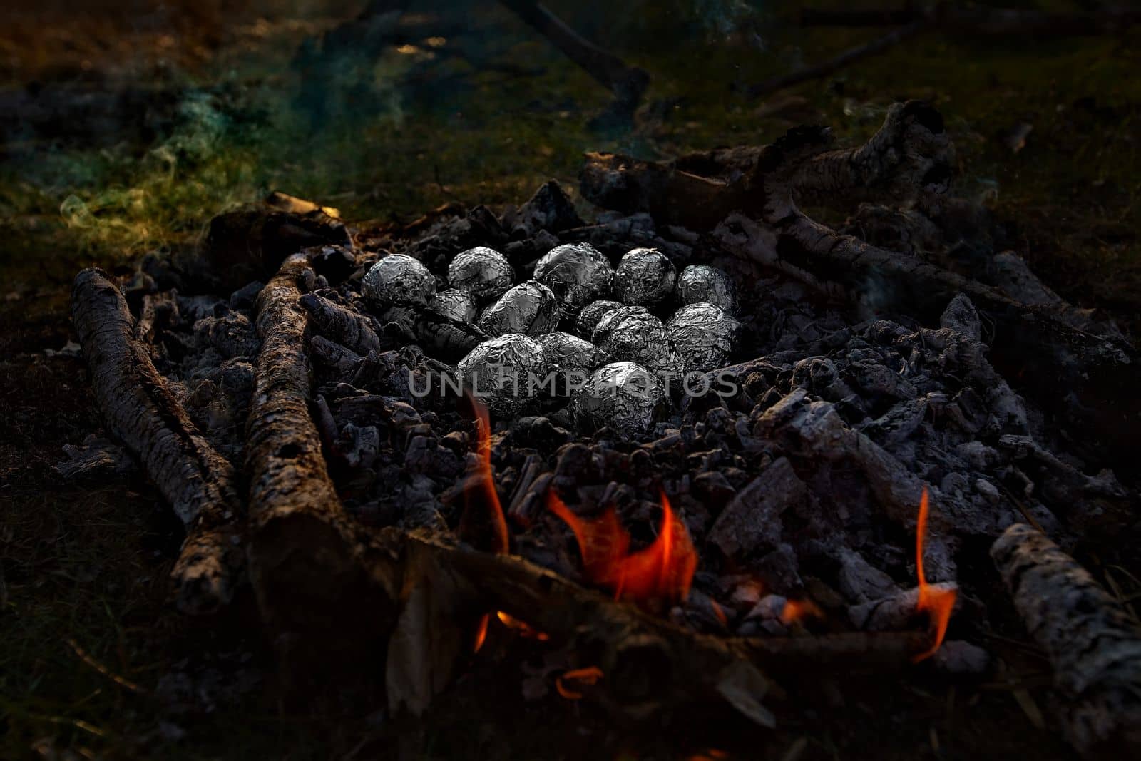 Fried potatoes wrapped in foil in a fire. The family, mother and daughter, for the weekend went out into the countryside for a picnic, sit by the fire in the wild with a tent, fry potatoes, drink hot tea. High quality photo