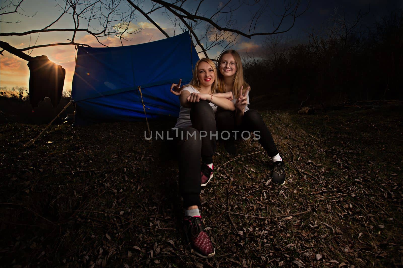 The family, mother and daughter, for the weekend went out into the countryside for a picnic, sit by the fire in the wild with a tent, fry potatoes, drink hot tea. High quality photo