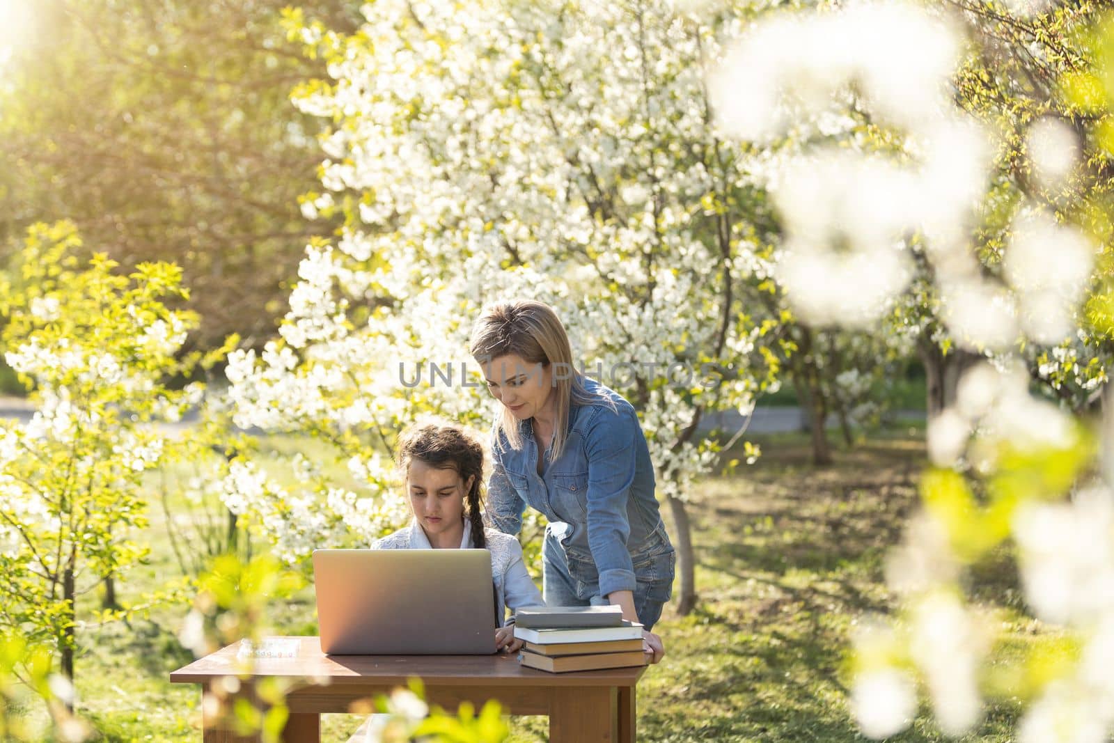 Woman and little girl laying on the spring flower field outdoors - having fun using a laptop
