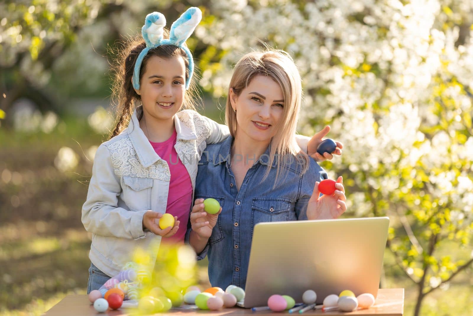 mother and daughter paint easter eggs with laptop.