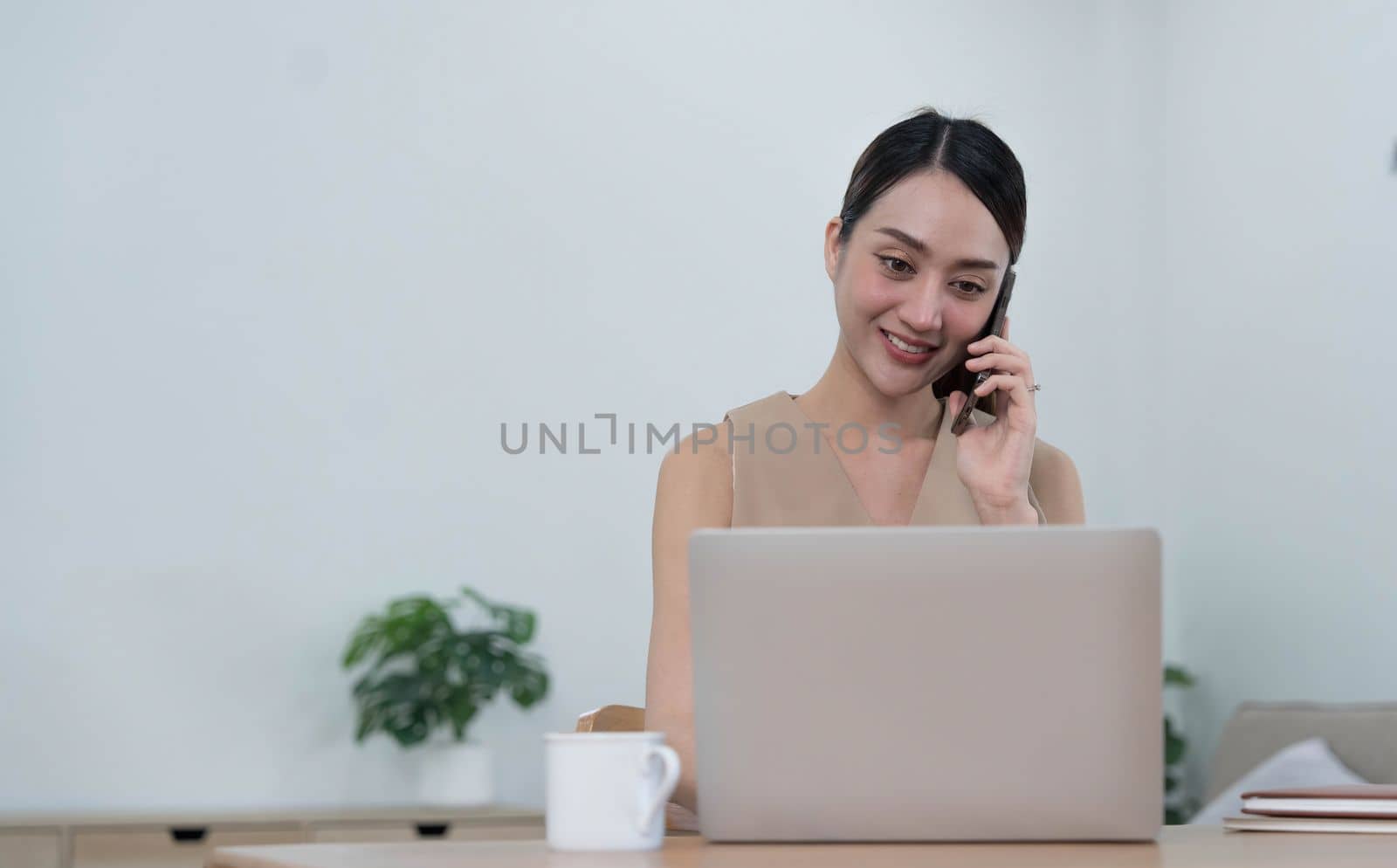 Smiling beautiful Asian businesswoman analyzing chart and graph showing changes on the market and holding smartphone at office. by wichayada