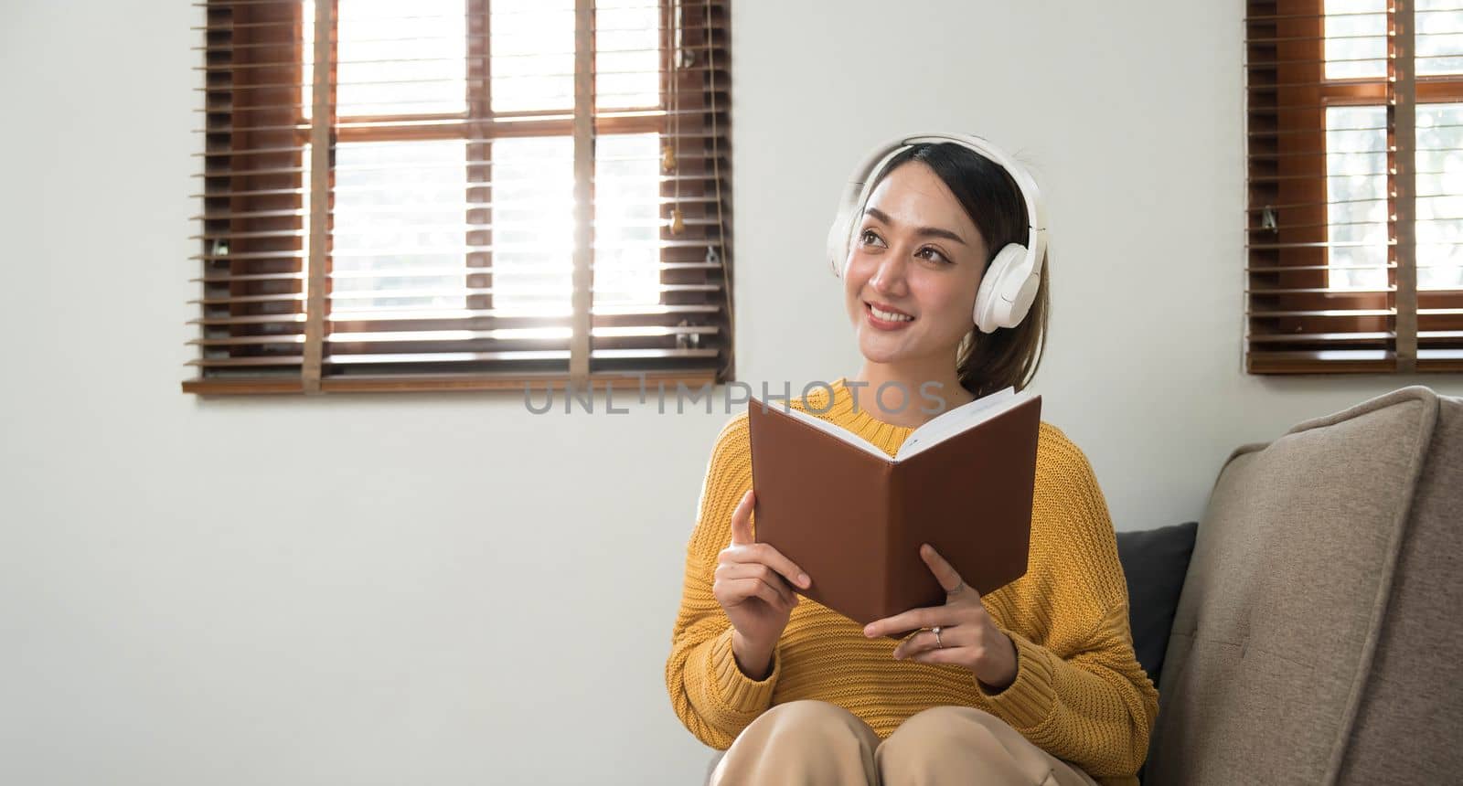 Smiling girl relaxing at home, she is playing music using a smartphone and wearing white headphones..