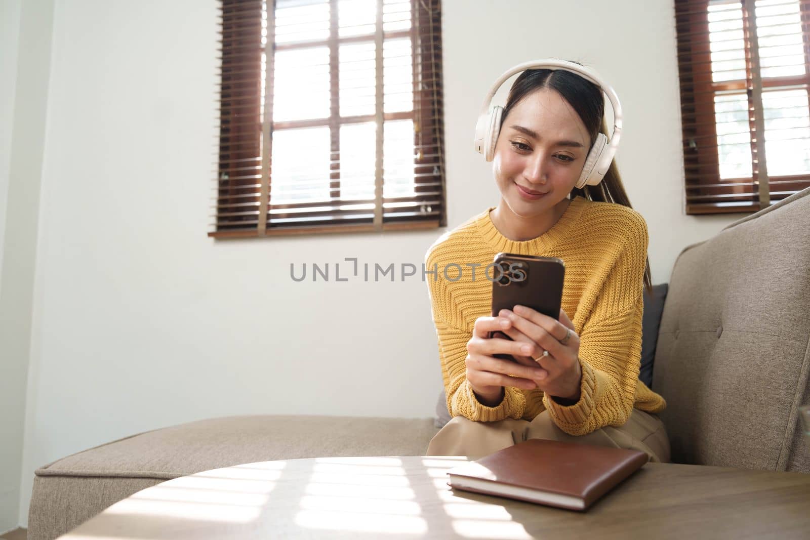 Smiling girl relaxing at home, she is playing music using a smartphone and wearing white headphones..