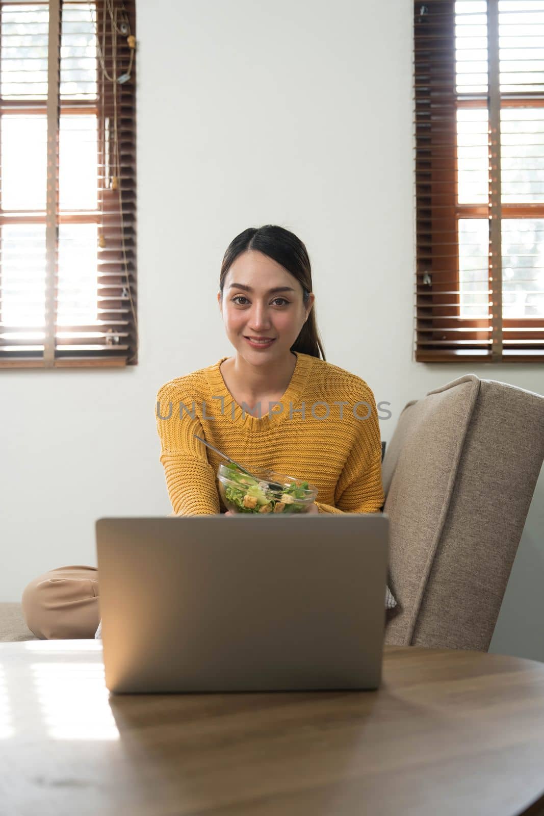 People relax at home and wellness lifestyle. Young adult asian woman eating salad and using laptop computer for watching online movie on internet...