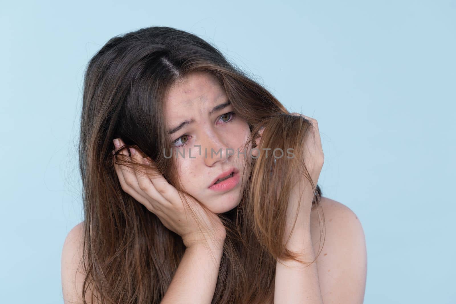 Beautiful girl feel sad, worry about her damaged hair with isolated background. Concept of dry lifeless hair. Young charming girl hold her tangled hair and look at it with worried expression.