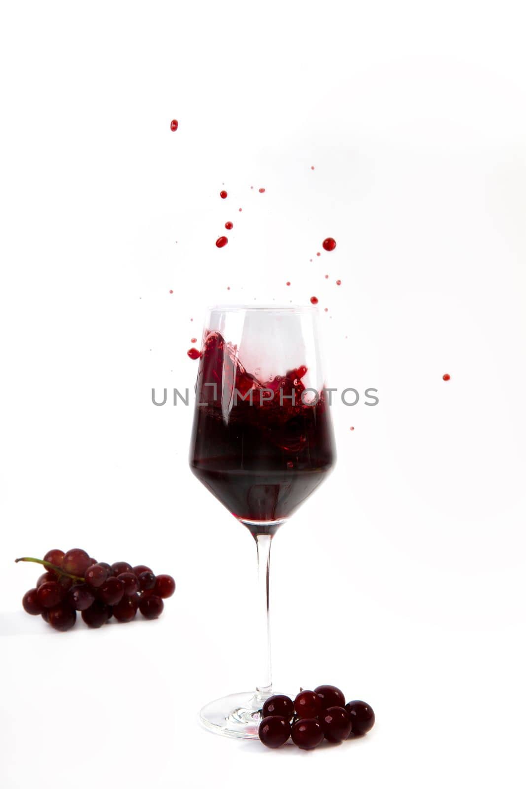 Wine Glass with a splash of red wine and grapes isolated on white background copy space by Annebel146