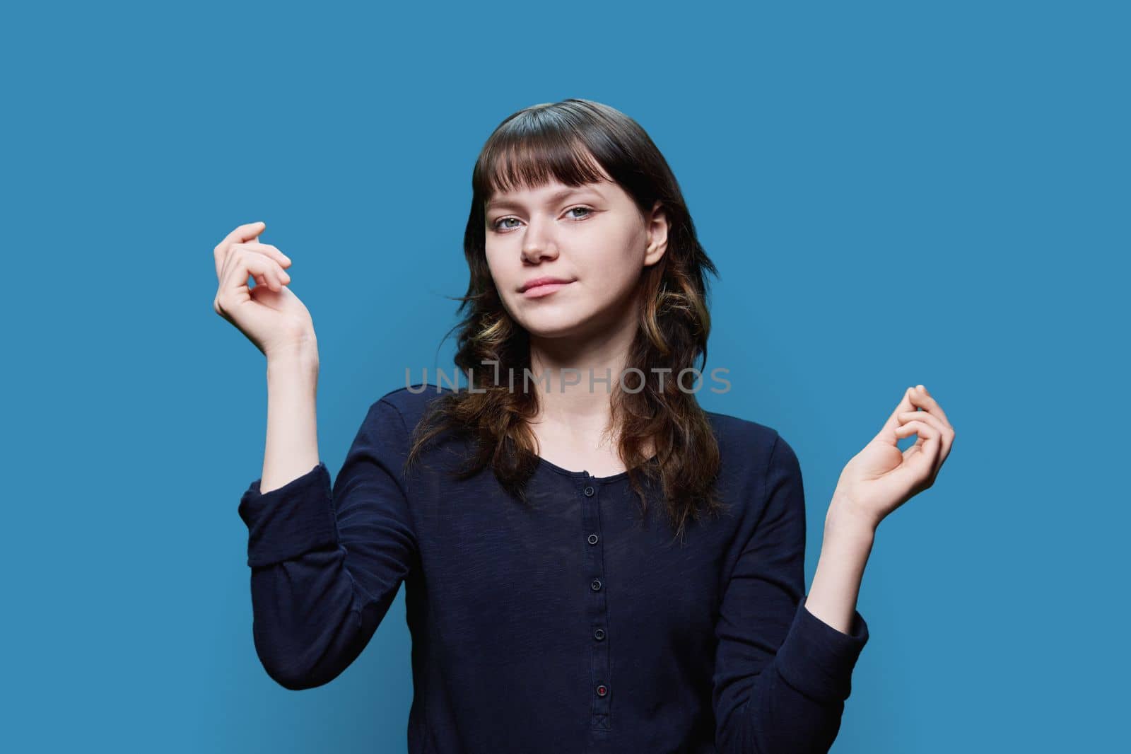 Young attractive female with hands up looking at camera on blue color studio background. Beauty, fashion, youth, positive emotions concept