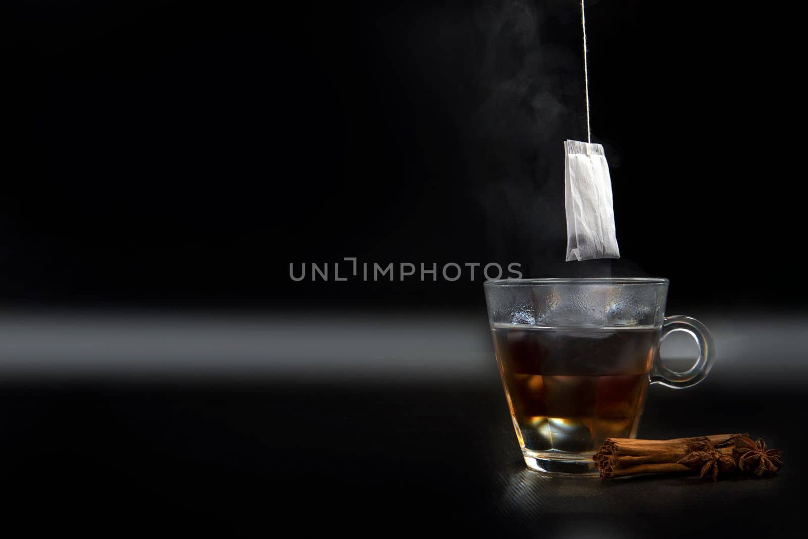 Glass of hot tea with tea bag hanging black background copy space, and cinnamon stick
