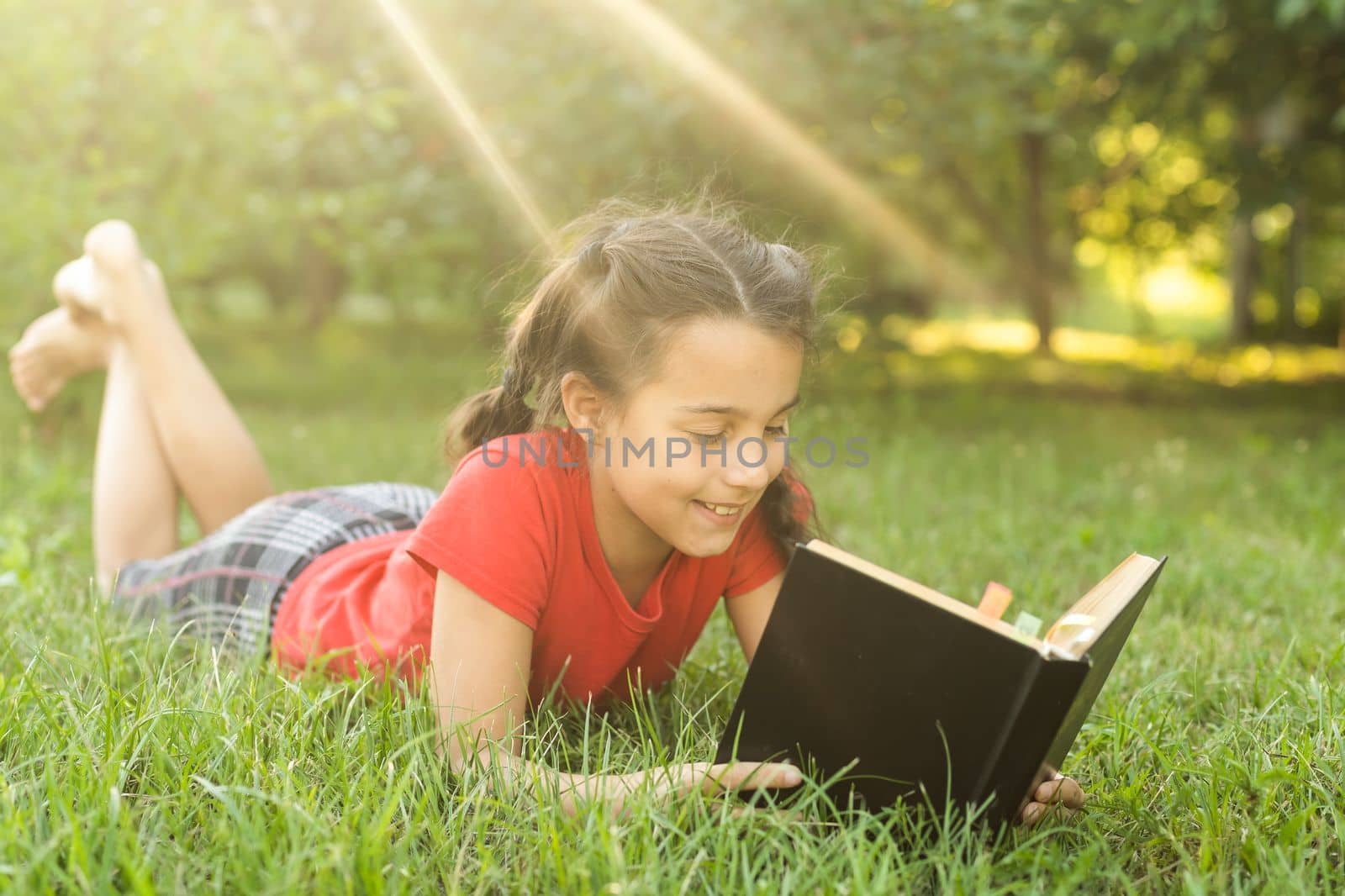 Little girl with a book in the garden. Kid is readding a book on hands. outdoors in summer day. Countryside.