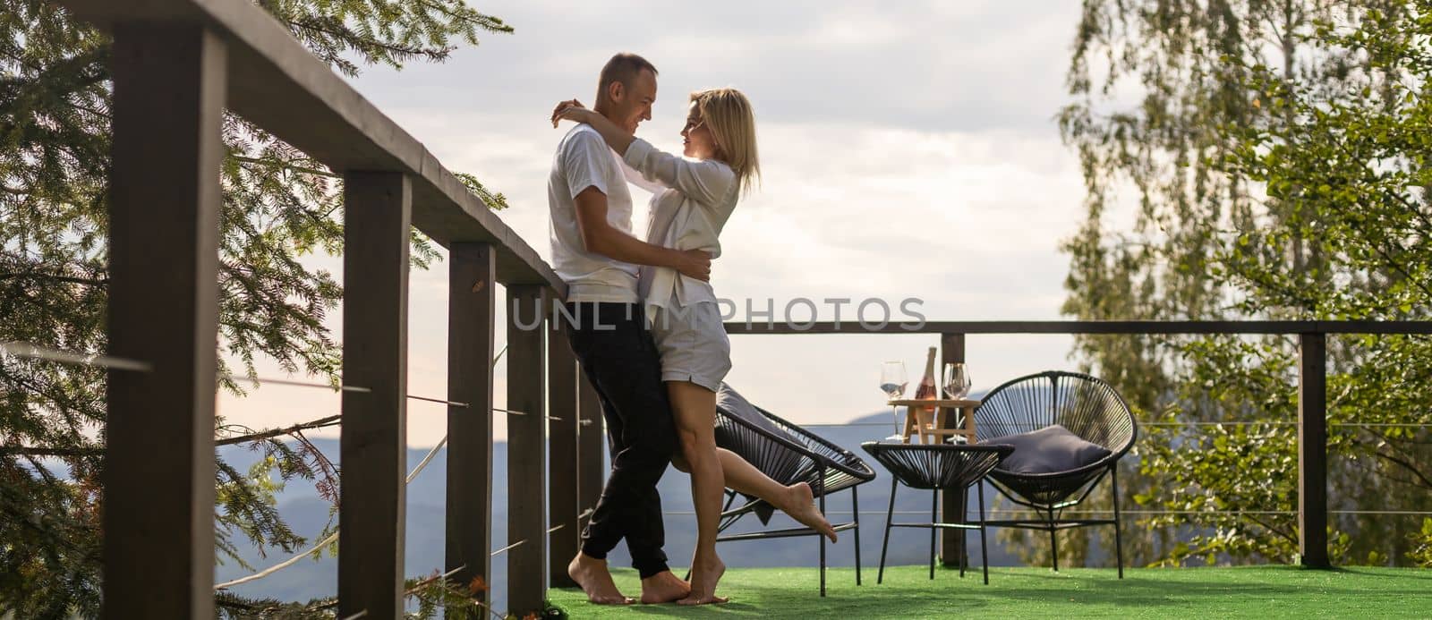 Horizontal sideview shot of a young couple in summer outfit enjoying the mountain view from terrace. Copy space