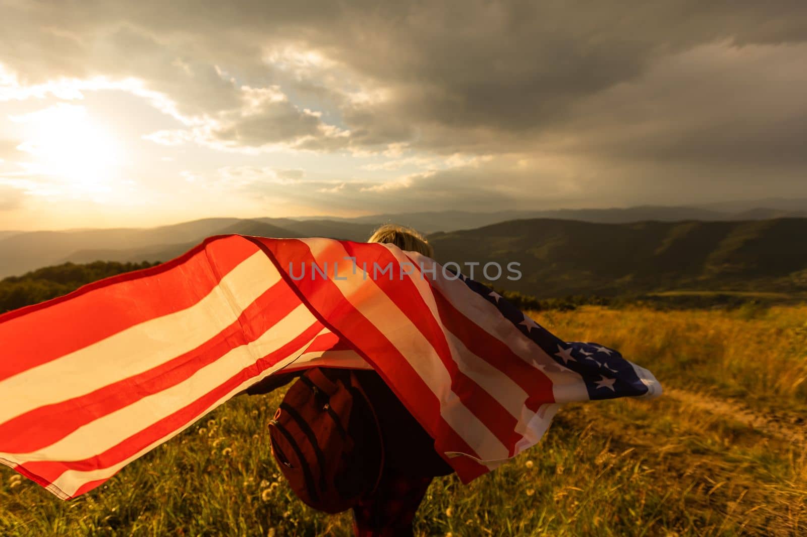 Young woman holding American flag on sky background.