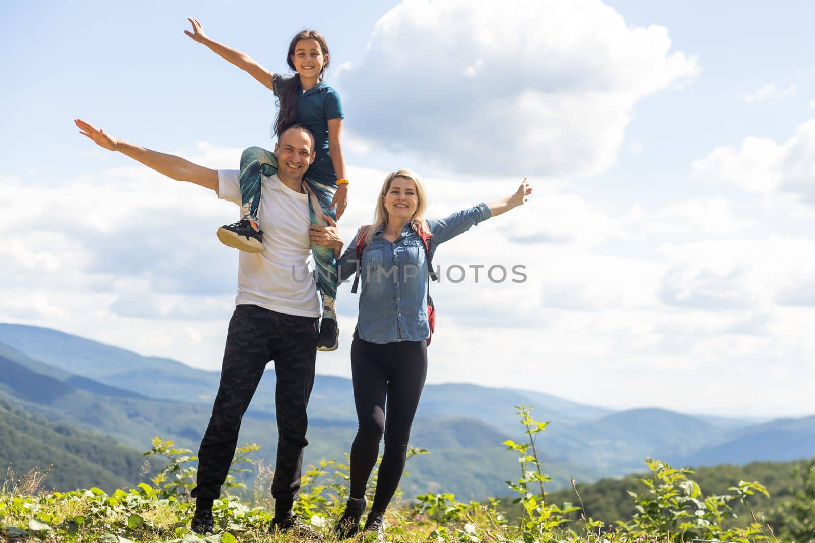 Mother, father hugging son, and daughter in summer mountains. Happy family smiling and standing on the green grass in the field at sunset. Kids with parents. Family weekend.