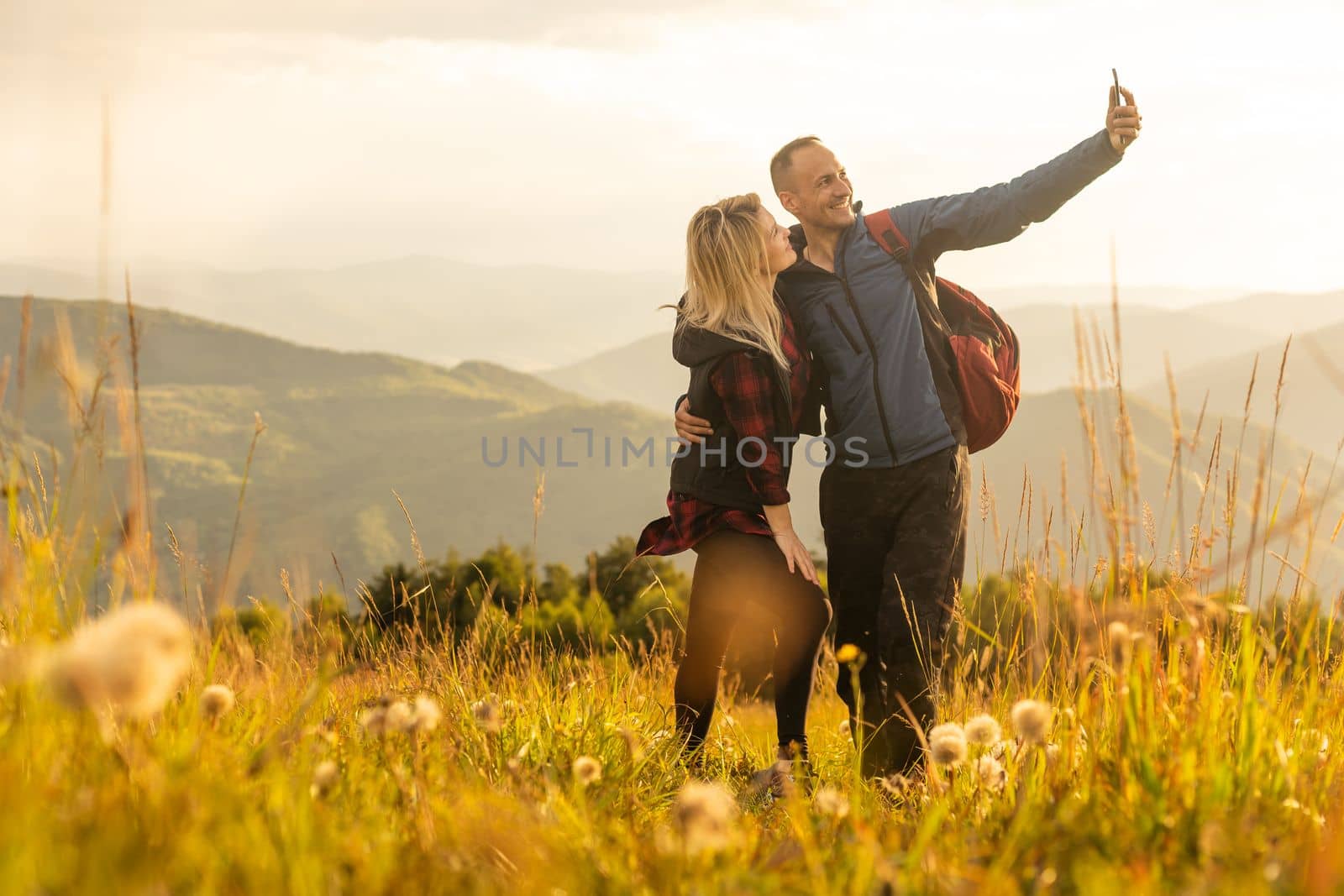 Man and woman standing and hugging on the top of the mountain, autumn hike with backpacks by Andelov13