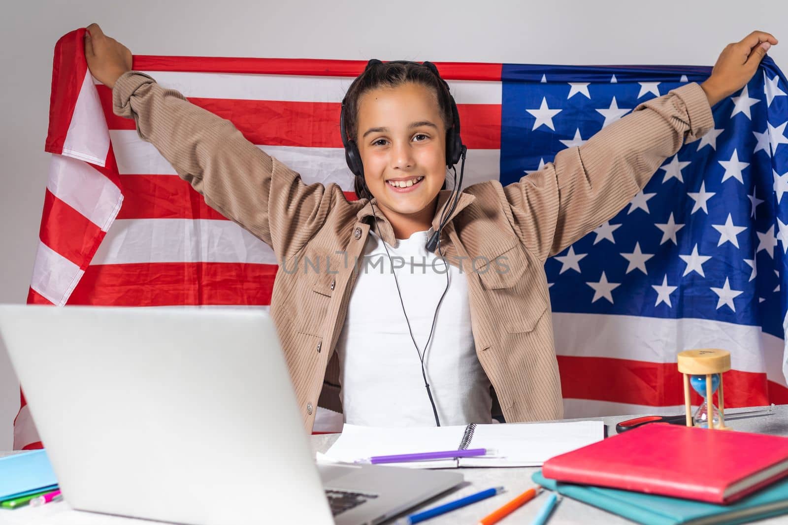 beautiful pupil sitting at desk and study online with laptop against background with USA flag