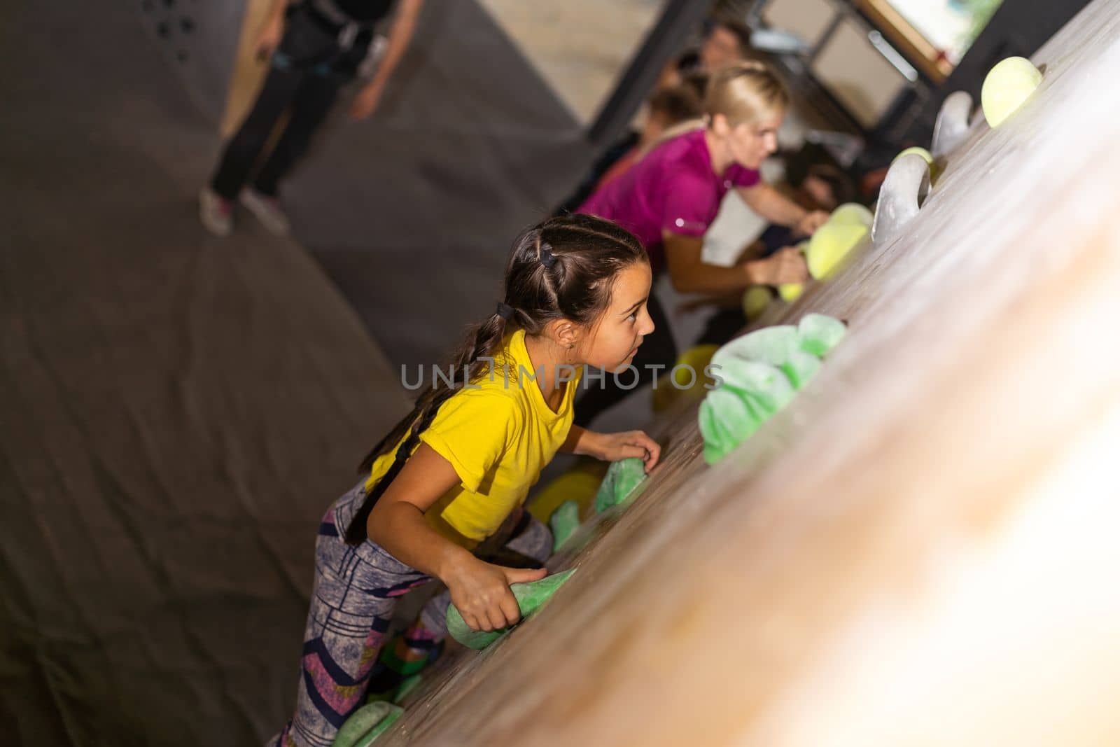 Young female bouldering instructor helping boy climb artificial wall by Andelov13
