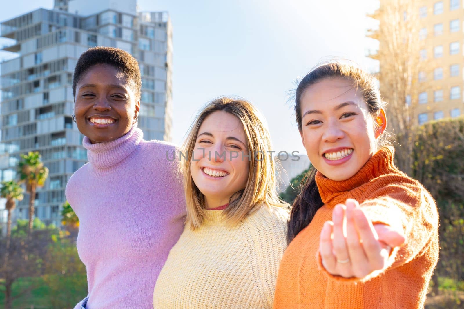 Portrait of some friends who embrace each other affectionately looking at the camera welcoming with her hand. Girls having fun in the city. Authentic people. High quality photo