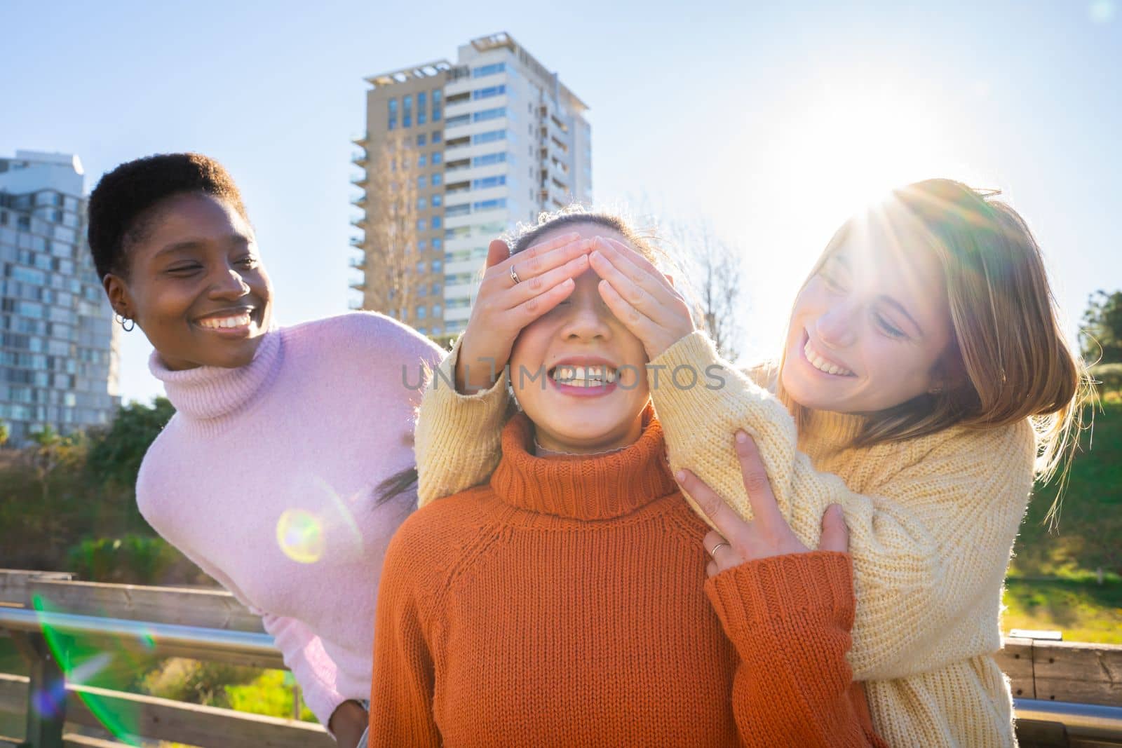 Female friends covering each other eyes for a surprise. Girls having fun together laughing. by PaulCarr