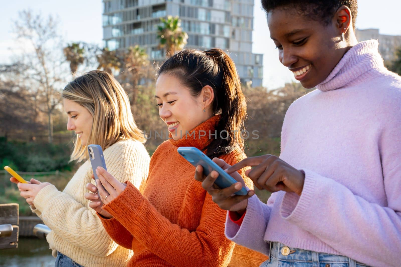 Cheerful female friends using cell phones. Technology addicted millennial community concept. by PaulCarr