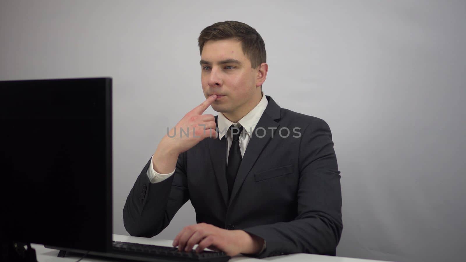 A young businessman is sitting in the office and typing on a computer keyboard. A man in a suit sits at a computer. 4k