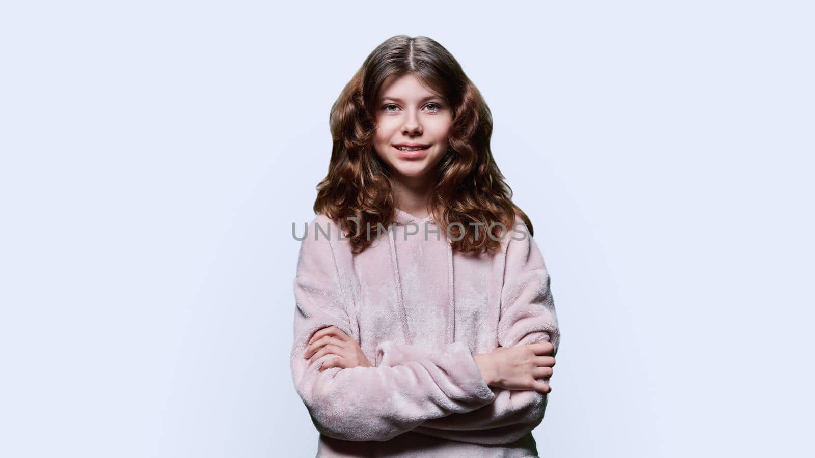 Portrait of smiling child schoolgirl on white studio background. Preteen girl looking at camera with crossed arms, wearing school clothes. School, kids, study education, childhood concept