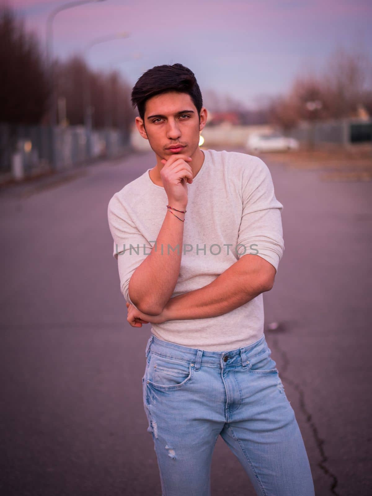 Handsome young man in white sweater outdoor in street, looking at camera