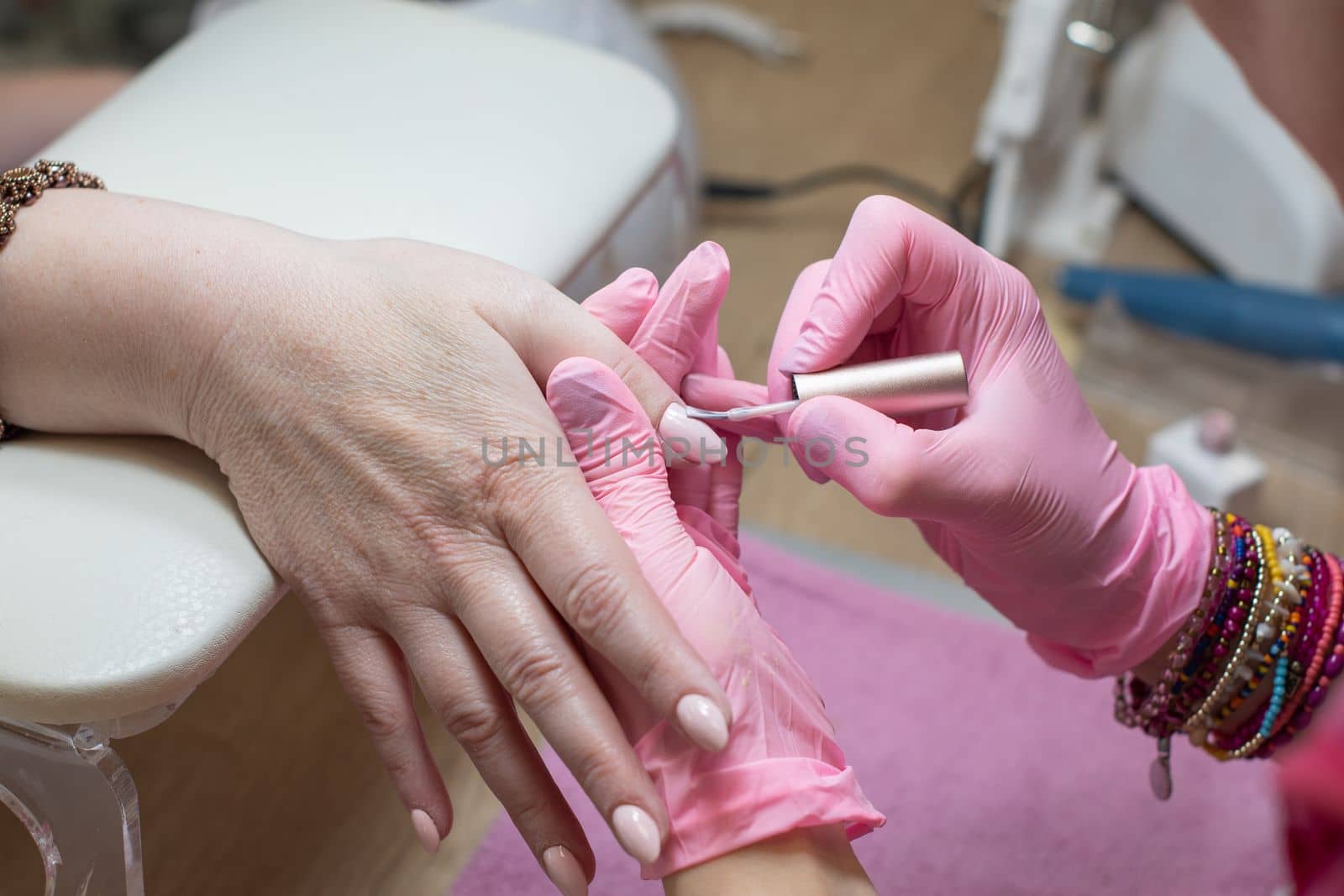 a master does a manicure to a client in a beauty salon and covers her nails with pink varnish. High quality photo