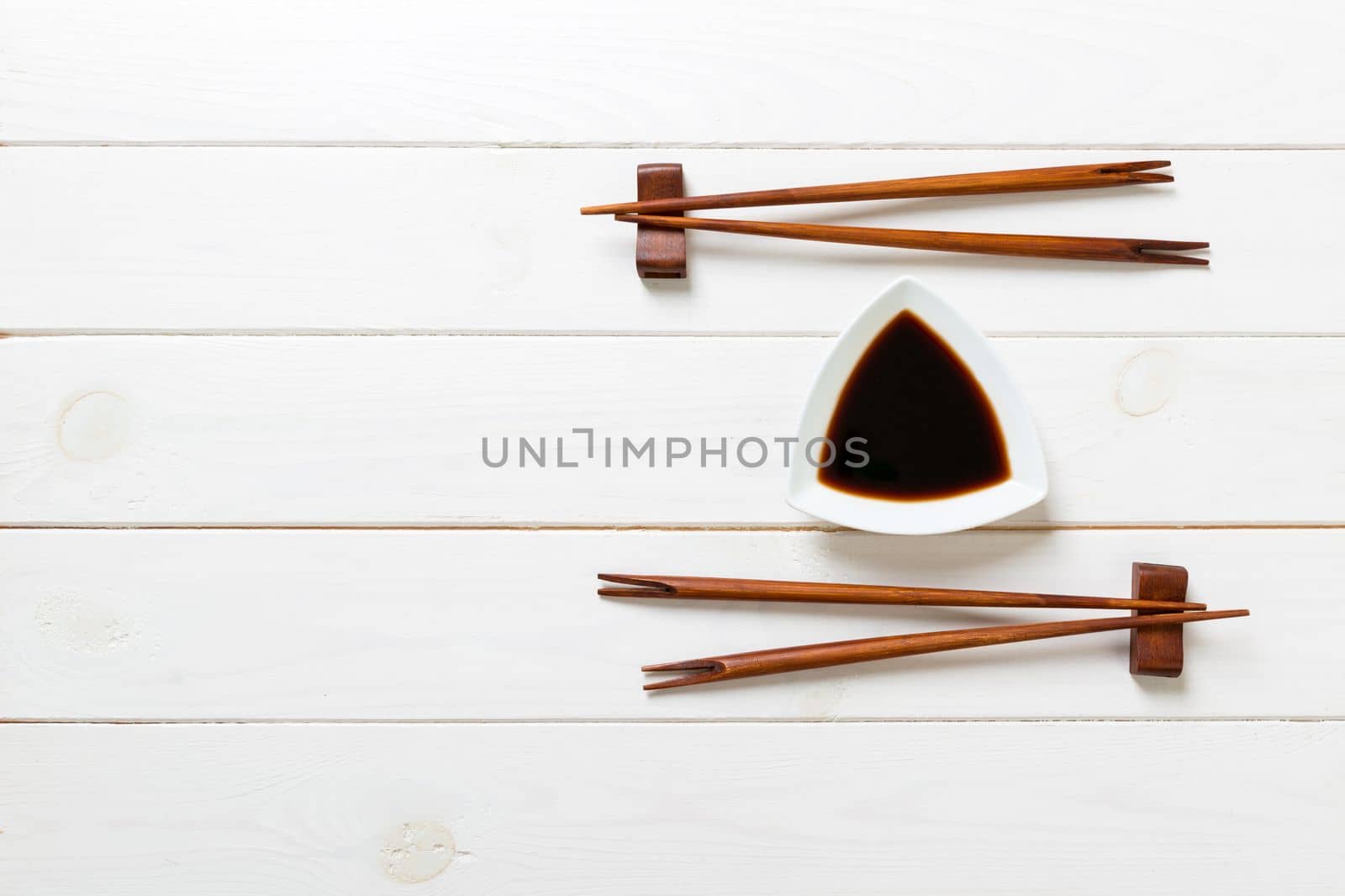Soy sauce with chopsticks on white wooden table background.