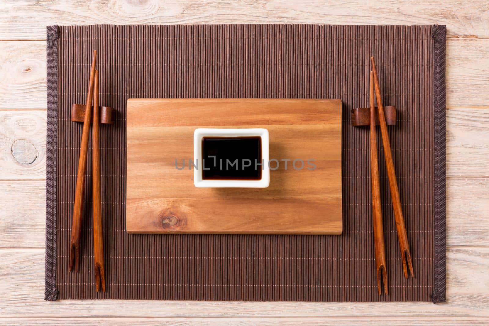 Empty rectangular wooden plate with chopsticks for sushi and soy sauce on wood background. Top view with copy space.