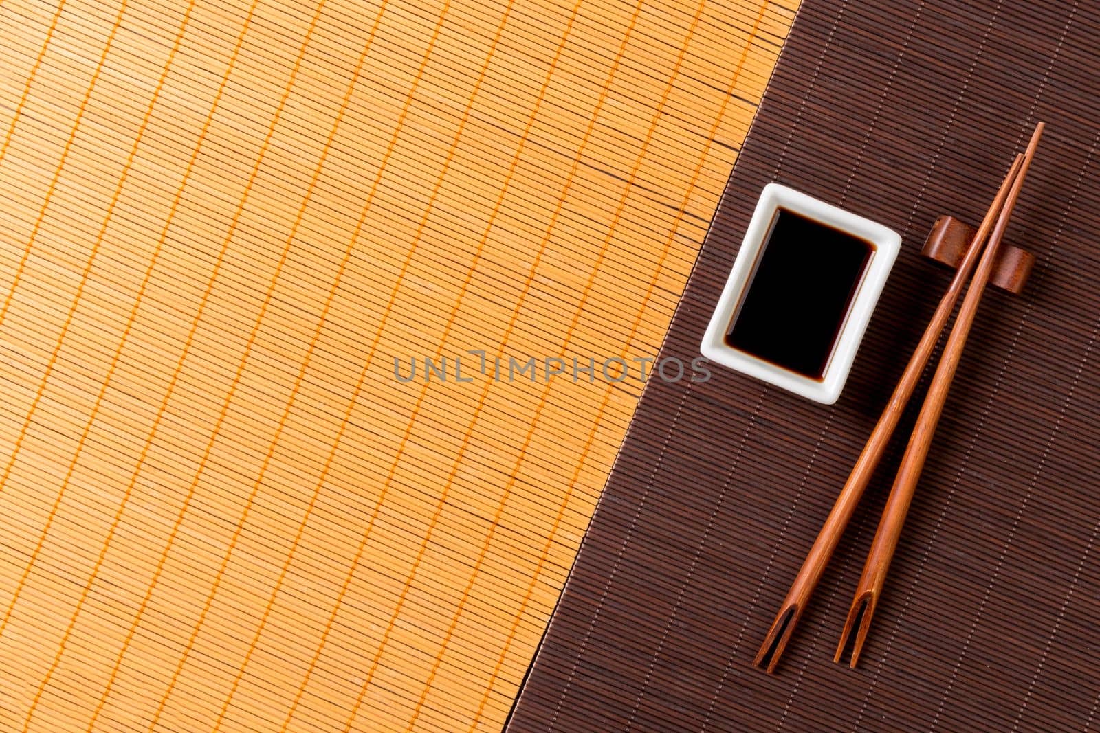 Chopsticks and bowl with soy sauce on two bamboo mat blak and yellow top view with copy space.