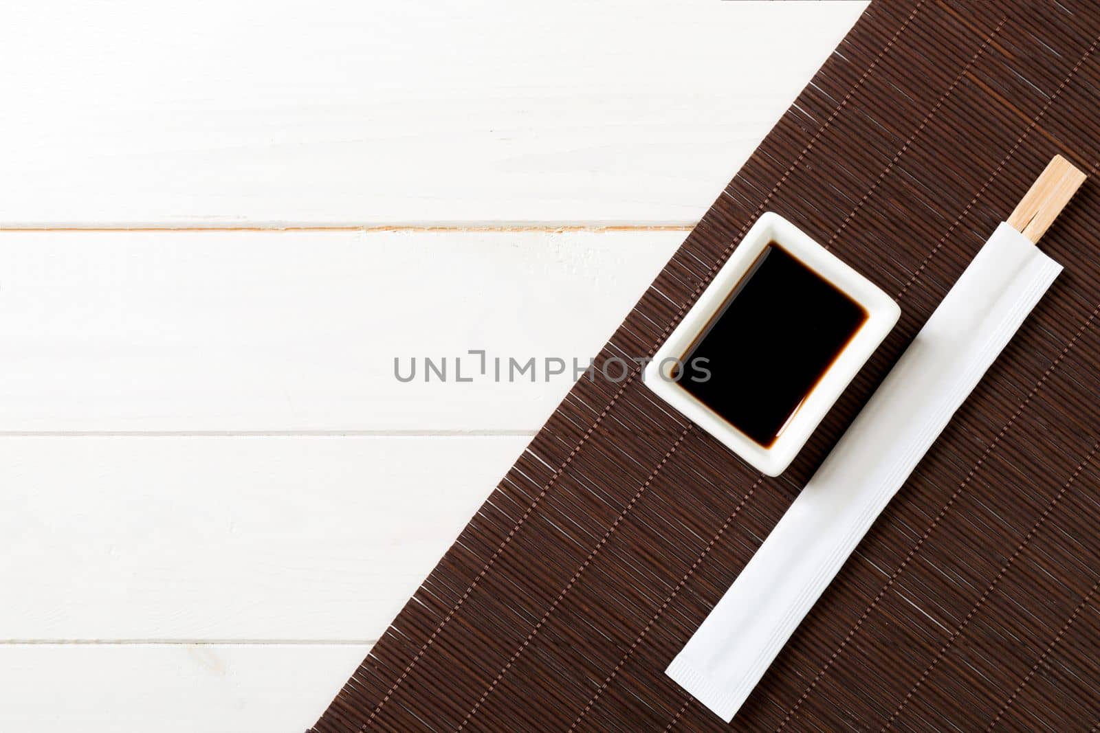 Bamboo mat and soy sauce with sushi chopsticks white on wooden table. Top view with copy space background for sushi. Flat lay