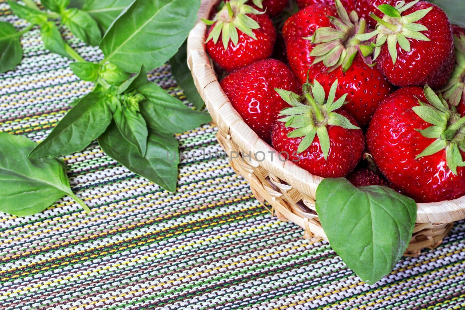Ripe sweet strawberries in wicker basket and mint leaves on wooden background