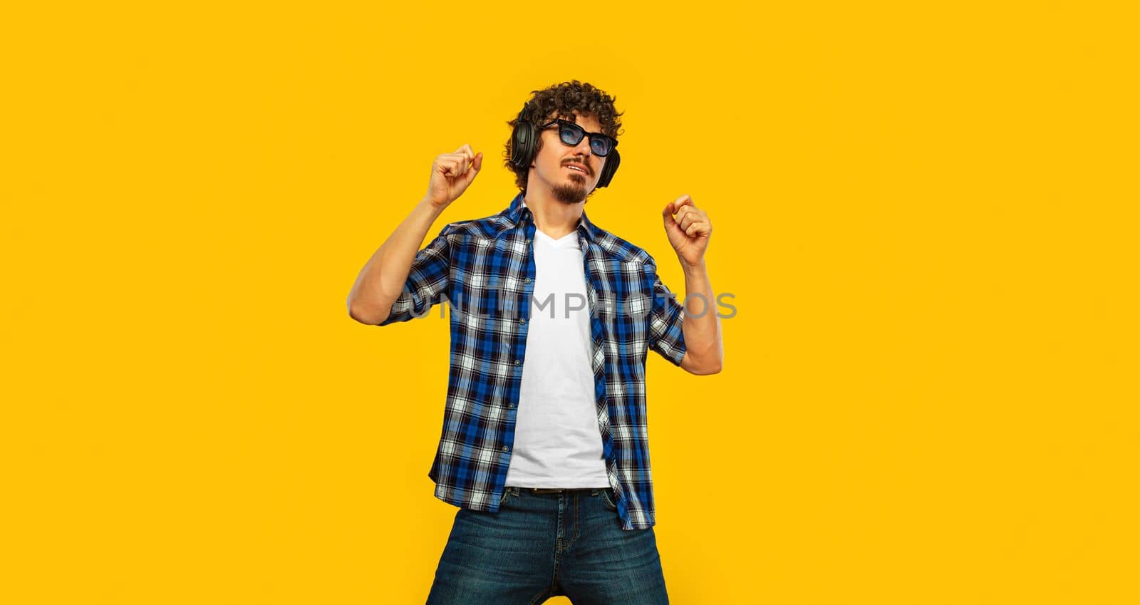 Handsome european man in yellow outfit smiling and dancing in excellent mood on blue background. Slow motion.