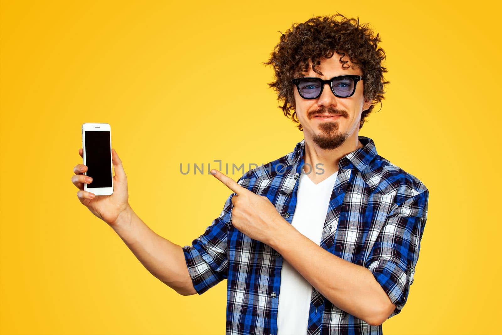 Handsome stylish man in hipster plaid shirt and sunglasses posing over yellow background