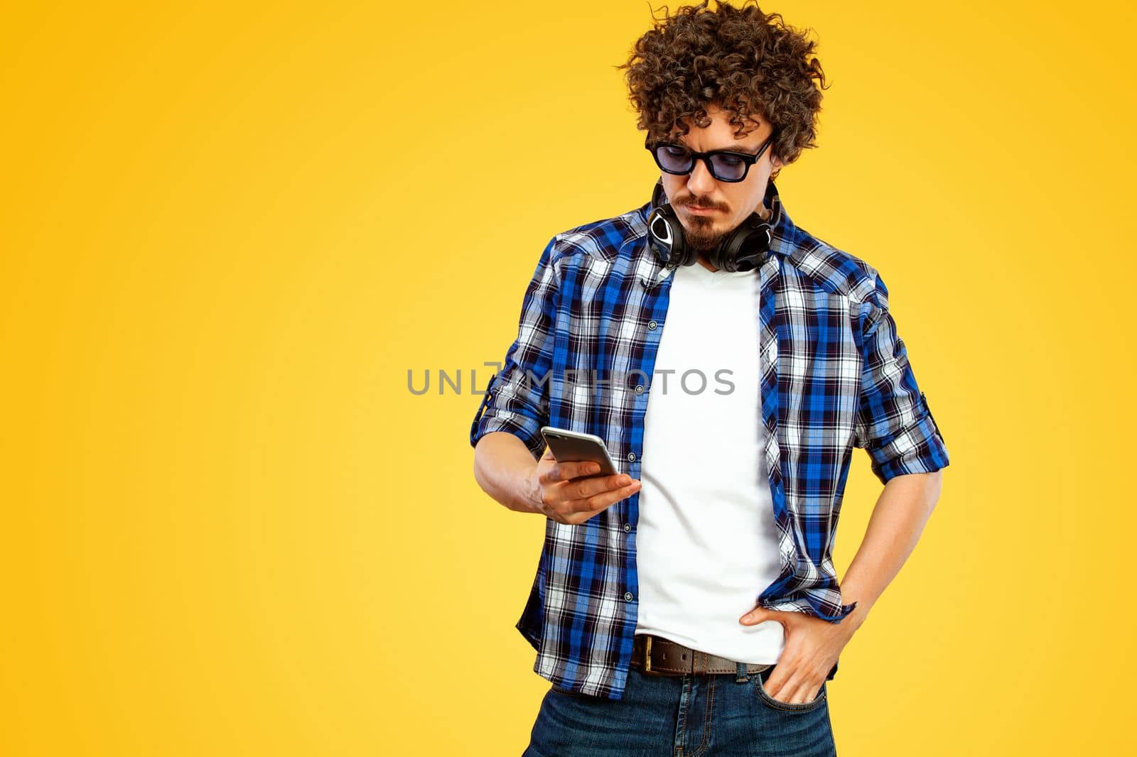 Handsome stylish man in hipster plaid shirt and sunglasses posing over yellow background