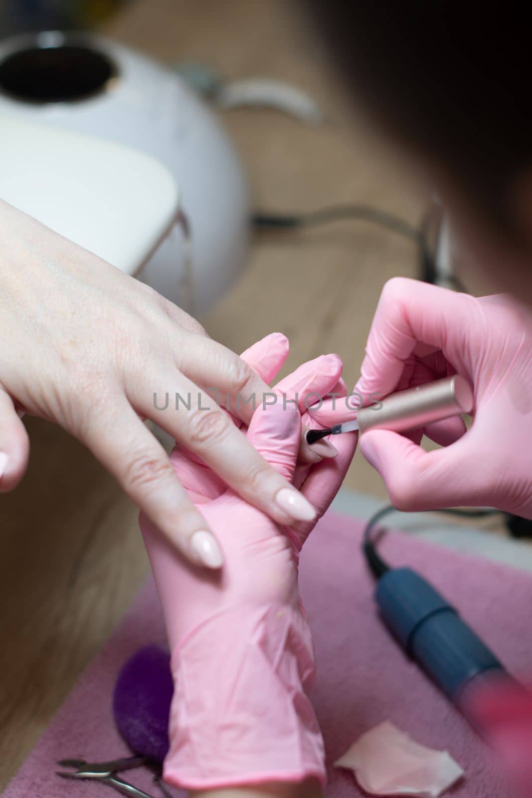 a master does a manicure to a client in a beauty salon and covers her nails with pink varnish. High quality photo