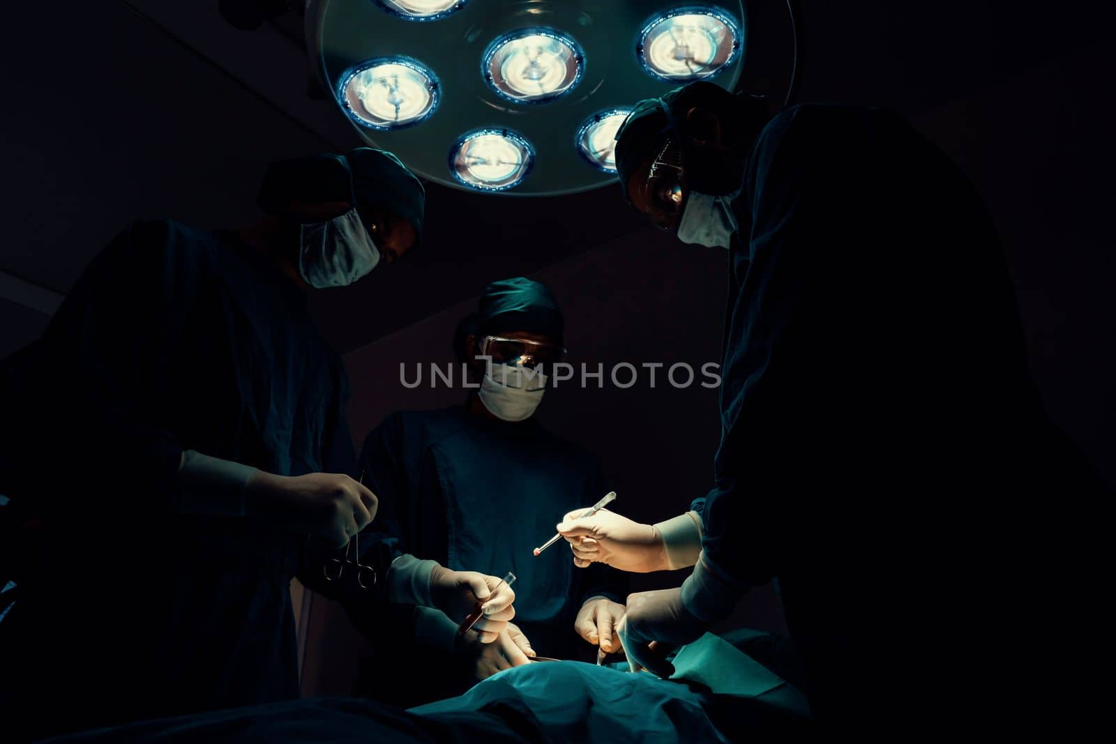 Surgical team performing surgery to patient in sterile operating room. by biancoblue